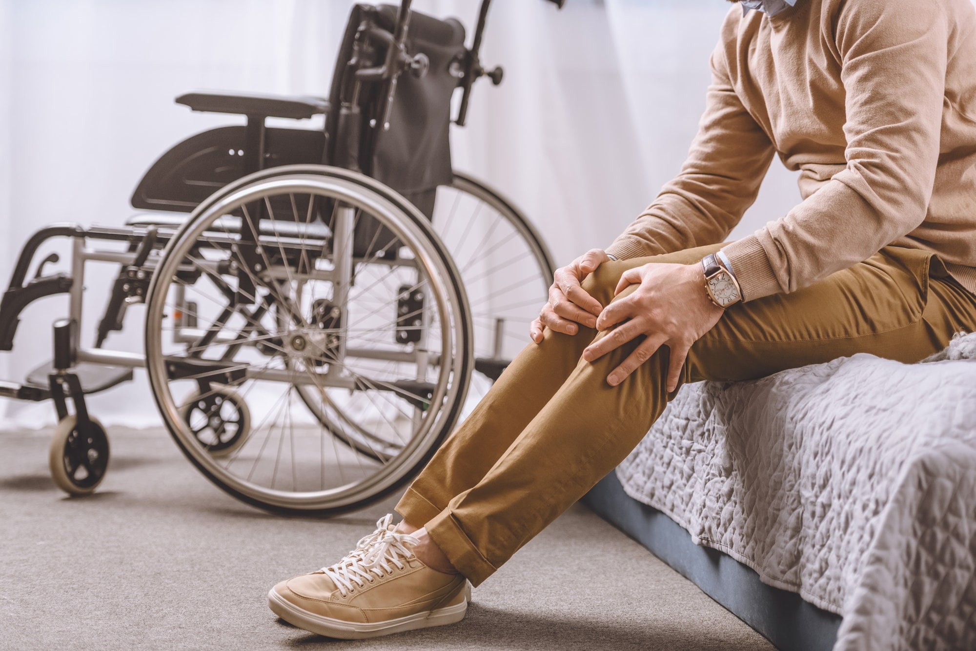 cropped image of man with disability sitting on bed and touching legs
