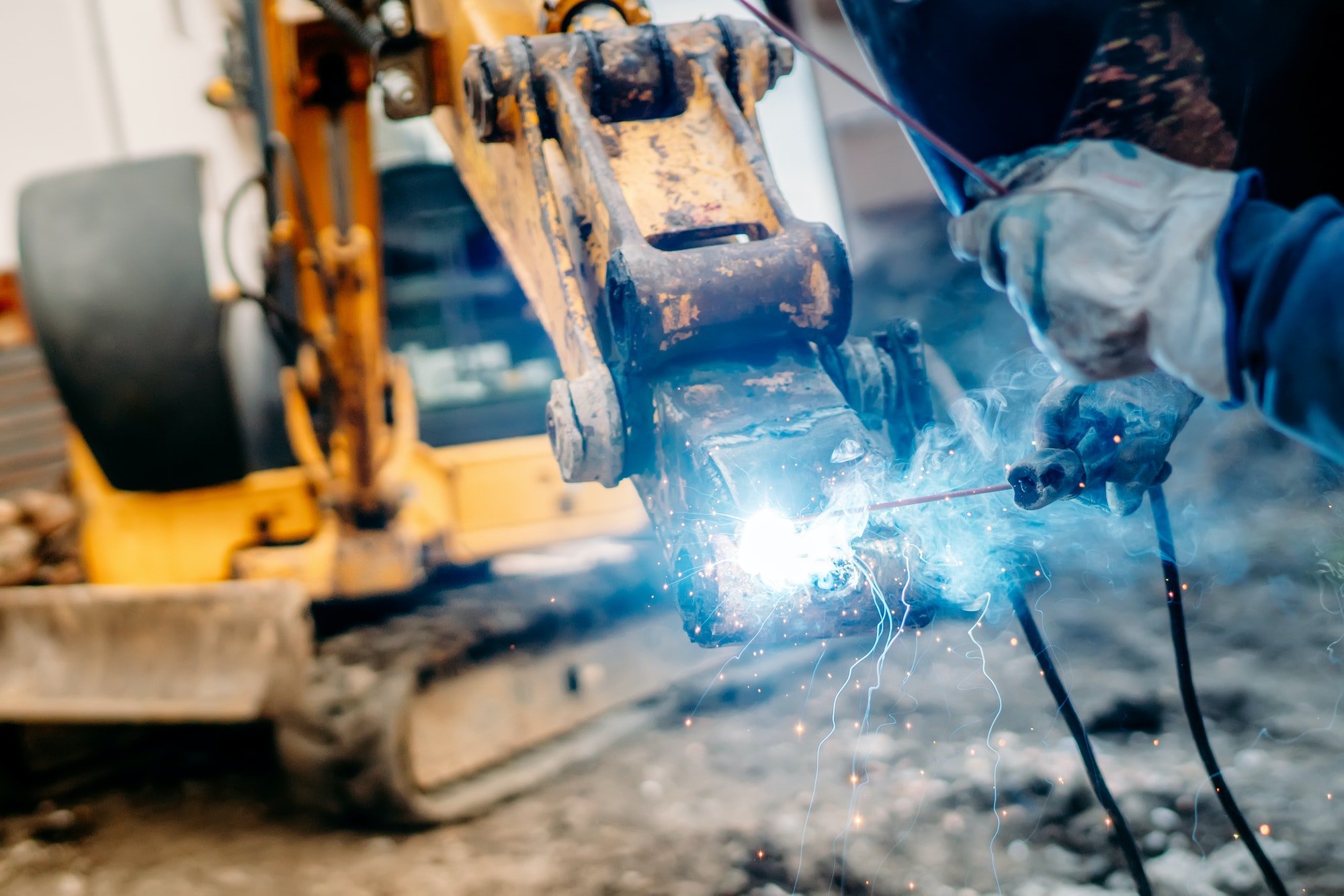 Industrial machinery being rapaired on construction site. mechanic welder working on excavator